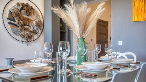 A dining table set with plates, glasses, and cutlery, a vase with pampas grass, and a wall art piece. - Balluta Harbour View (St Julian`s)