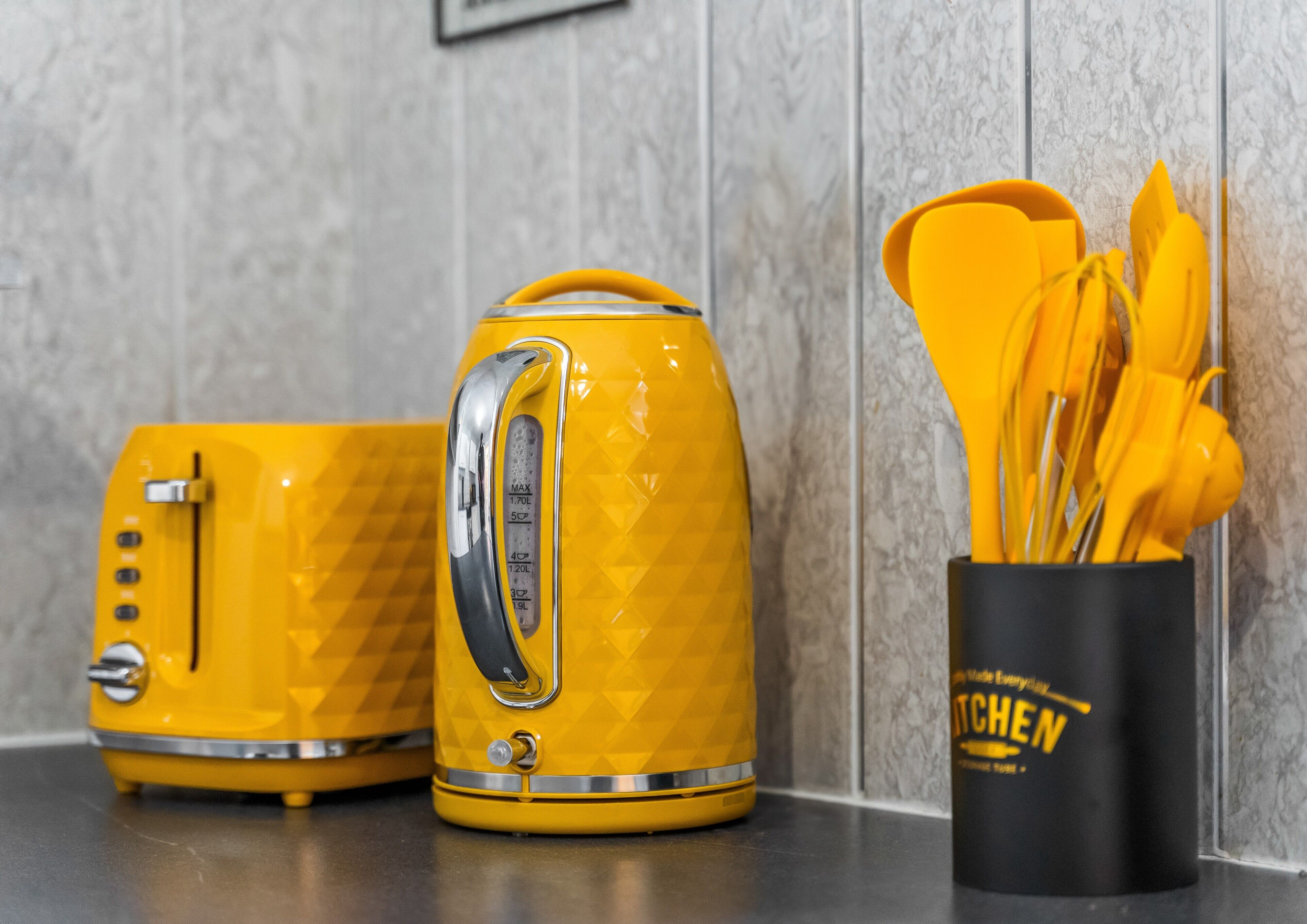 A yellow electric kettle and toaster on a countertop with a black mug containing yellow utensils.
