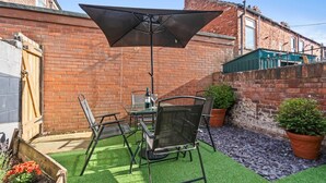Une terrasse avec une table et des chaises, un grand parasol et des plantes en pot.