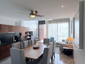 Ein modernes Wohnzimmer mit Essbereich, einer Küche und einem großen Fenster mit Vorhängen.