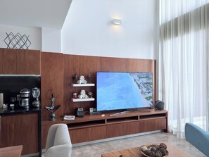 Ein modernes Wohnzimmer mit Flachbildfernseher, Holzschränken, einer Kaffeestation und einem Essbereich.