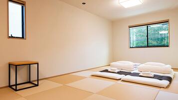 A room with tatami flooring, a bed with white bedding, a small table, and two windows.