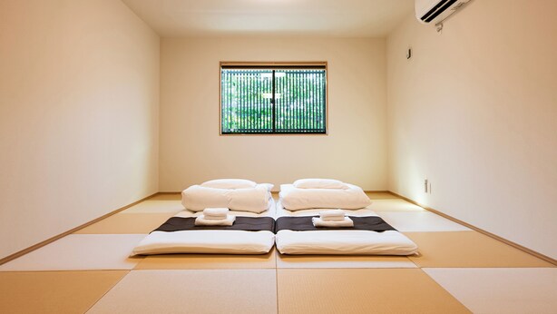 A room with tatami mats, two beds with white bedding, a window with vertical blinds, and an air conditioning unit on the wall. - Irodori Hotel KAZE (fukuokashi,hakataku,toukou)