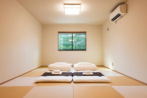 A room with tatami mats, two beds with white bedding, a window with vertical blinds, and an air conditioning unit on the wall. - Irodori Hotel KAZE (fukuokashi,hakataku,toukou)
