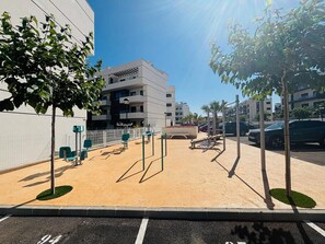 Ein Spielplatz mit Trainingsgeräten, ein mehrstöckiges Gebäude und geparkte Autos.