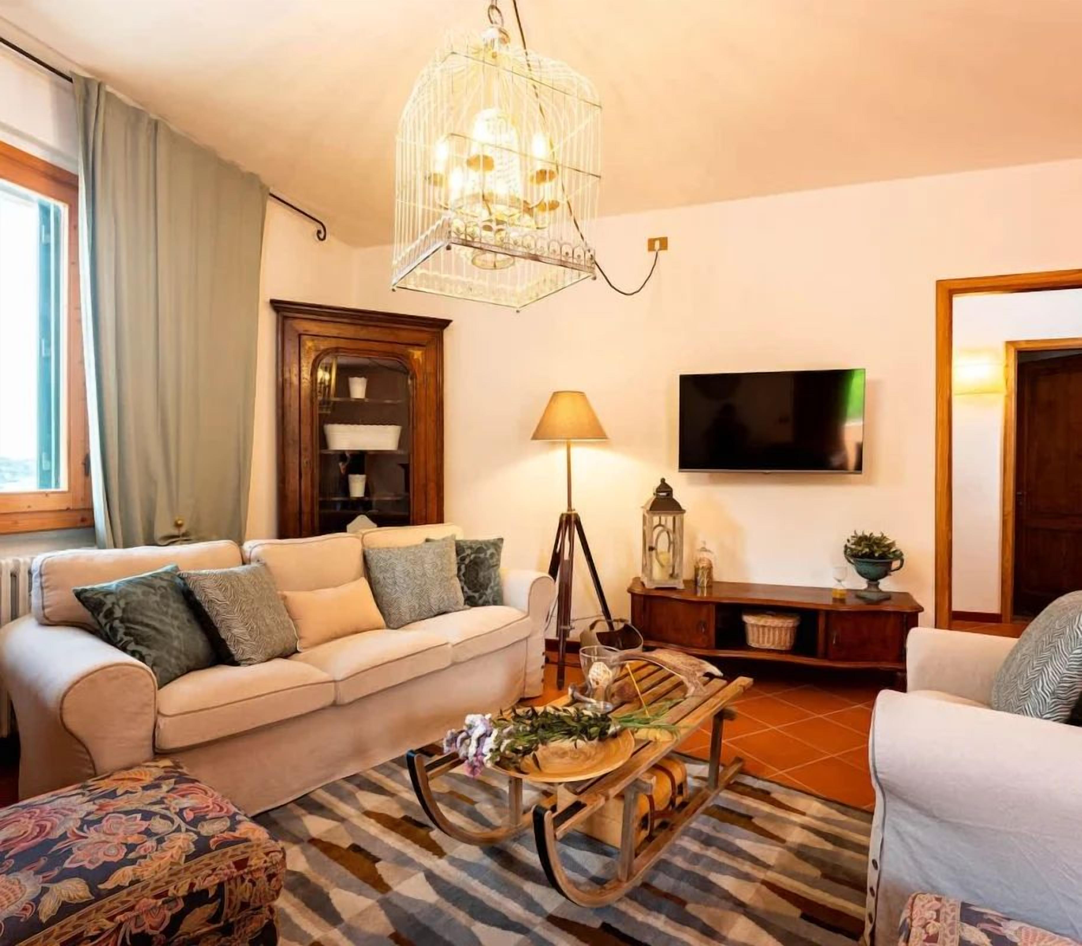 Een woonkamer met een bank, een salontafel, een lamp, een televisietoestel en een decoratieve vogelkooi.