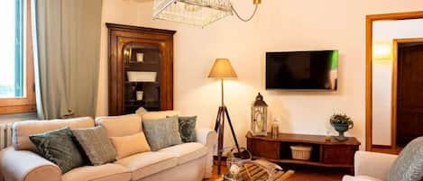 Een woonkamer met een bank, een salontafel, een lamp, een televisietoestel en een decoratieve vogelkooi.