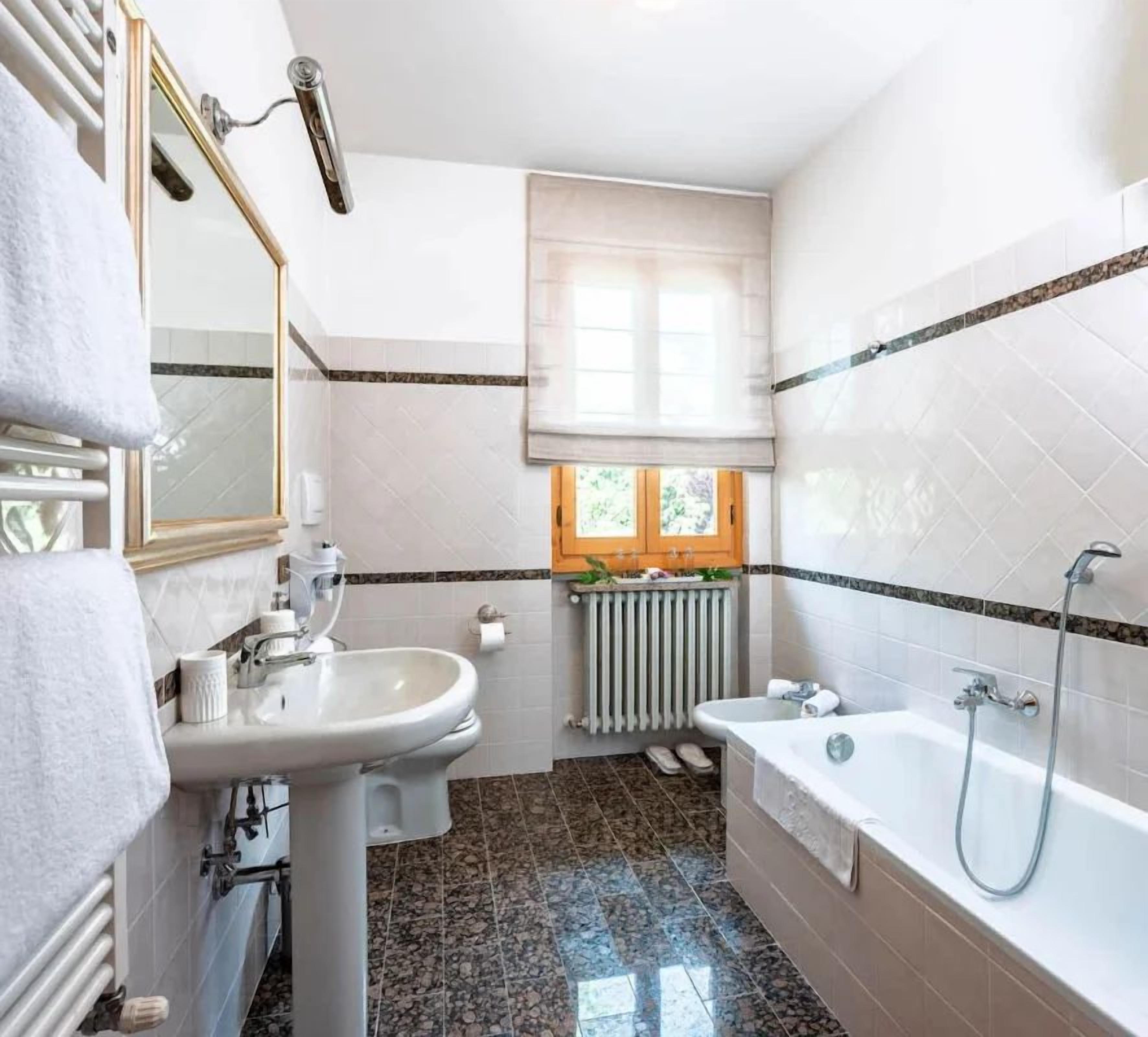 A bathroom with a sink, mirror, towel rack, window, radiator, and bathtub.