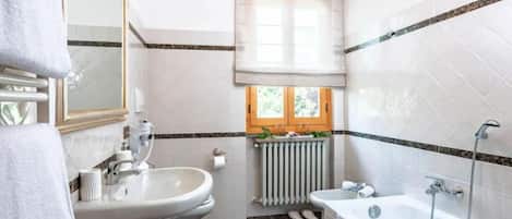 A bathroom with a sink, mirror, towel rack, window, radiator, and bathtub.