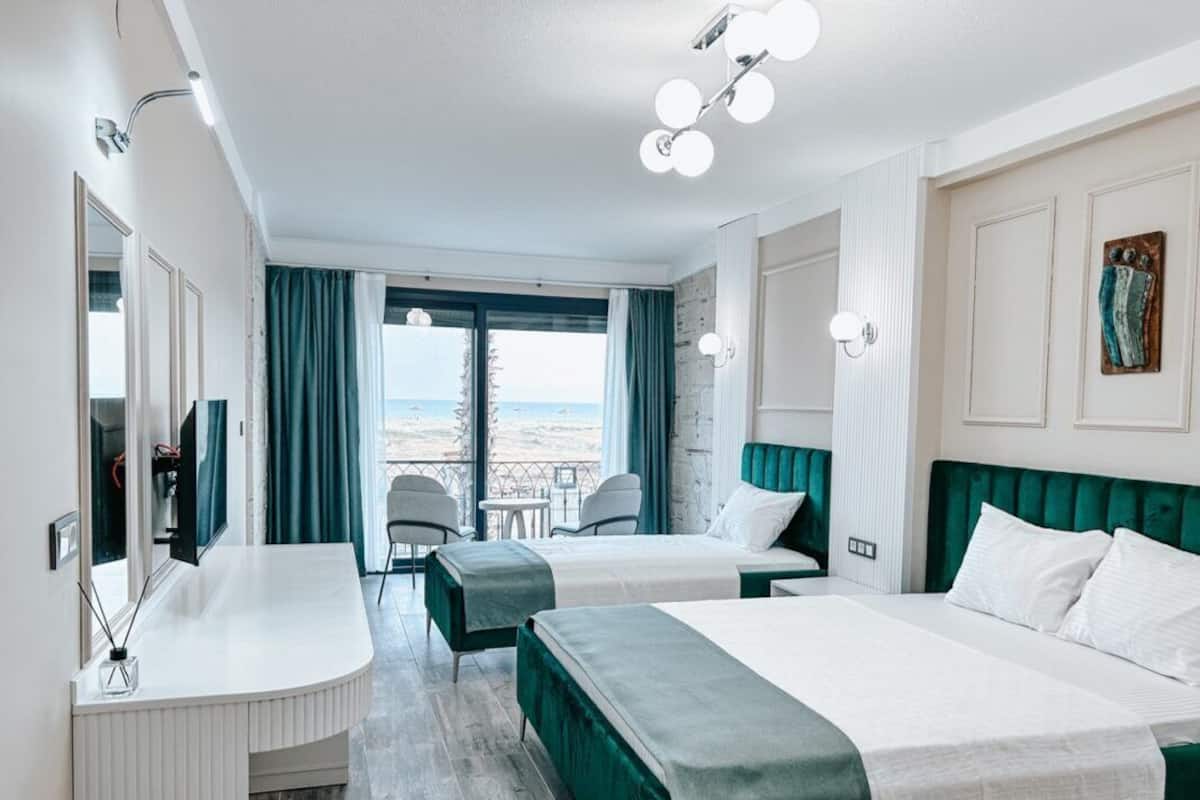 A hotel room with two beds, a vanity with a mirror, a chair, and a view of the beach.