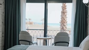 A hotel room with a bed, two chairs, a small table, and a view of the beach. - one lıfe otel (Ayvalık)