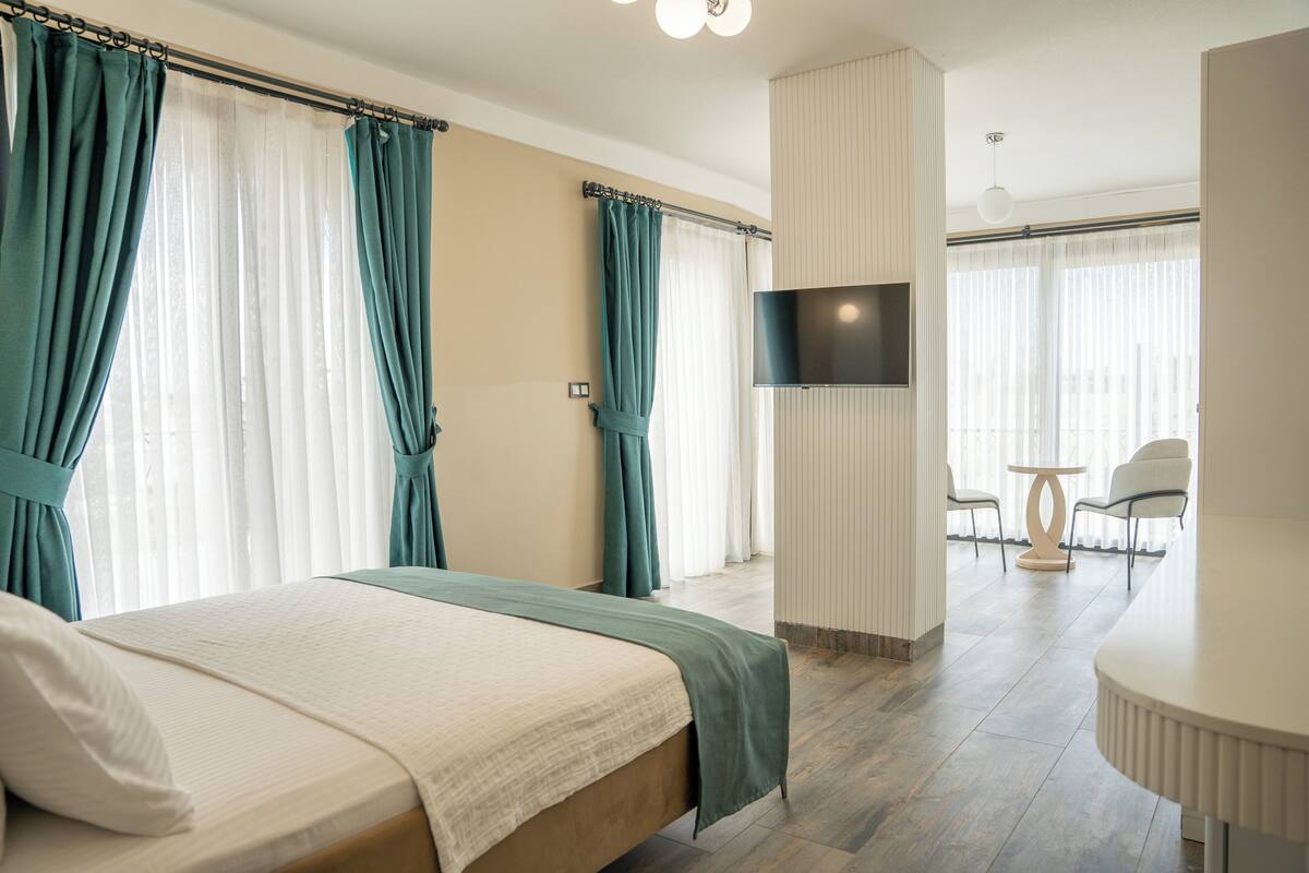 A hotel room with a bed, curtains, a TV, a small table, and chairs.