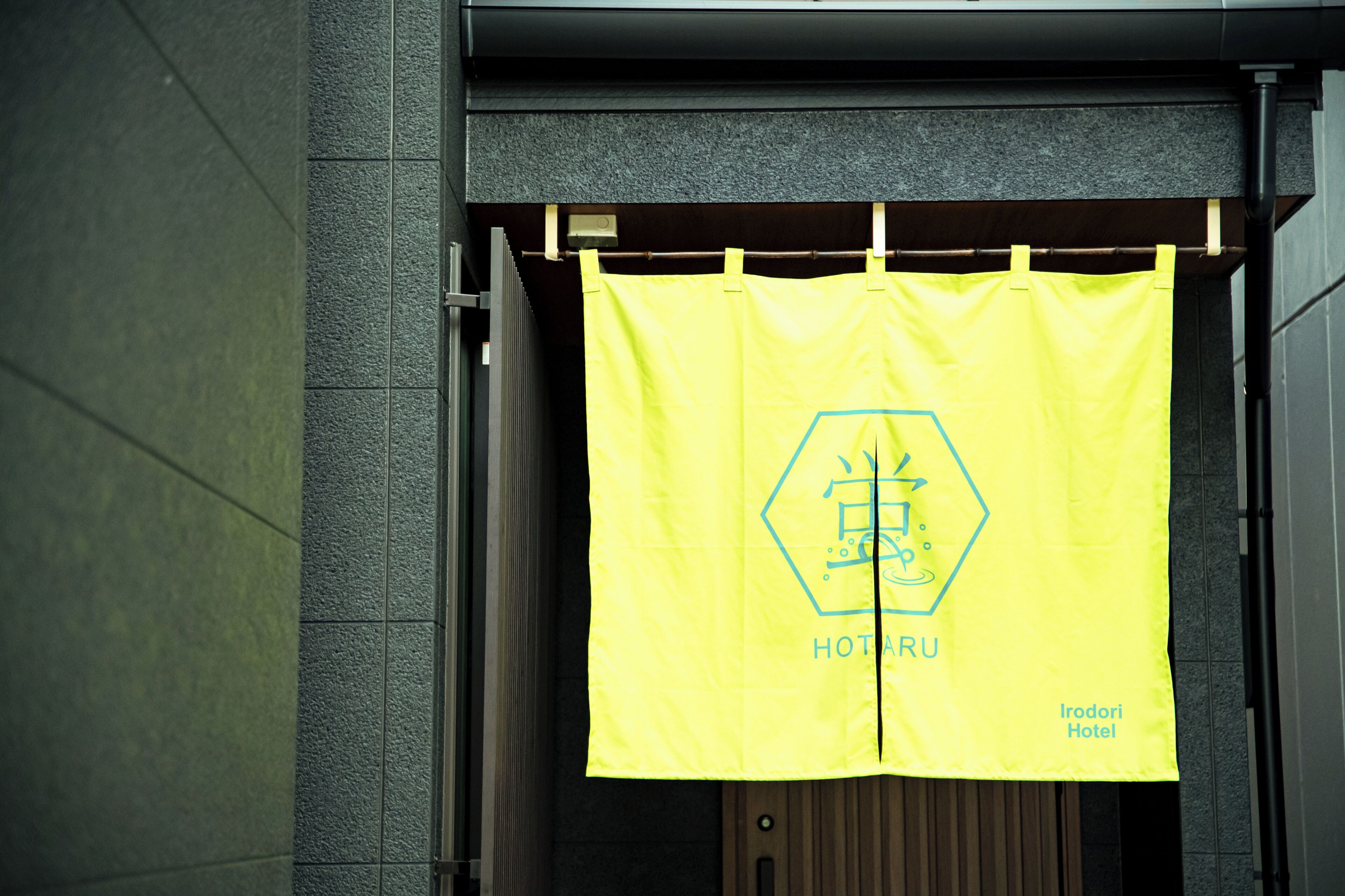 A yellow banner with a hexagonal logo and the text 'HOTARU Irodori Hotel' hanging on a building entrance.