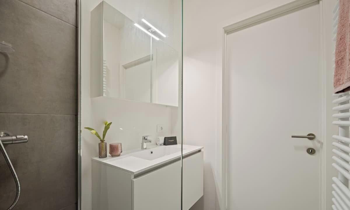 Ein modernes Badezimmer mit einer Duschkabine aus Glas, einem weißen Waschbecken und einer Tür mit Handtuchhalter.