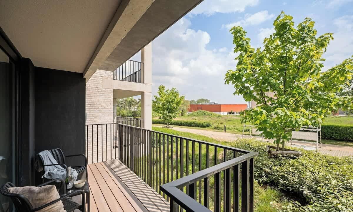 Ein Balkon mit Blick auf eine angelegte Grünfläche, einen Baum und ein Gebäude im Hintergrund.