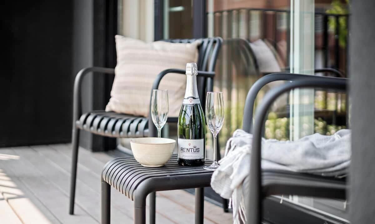 A balcony with a table set for two, featuring a bottle of wine, two glasses, and a bowl.