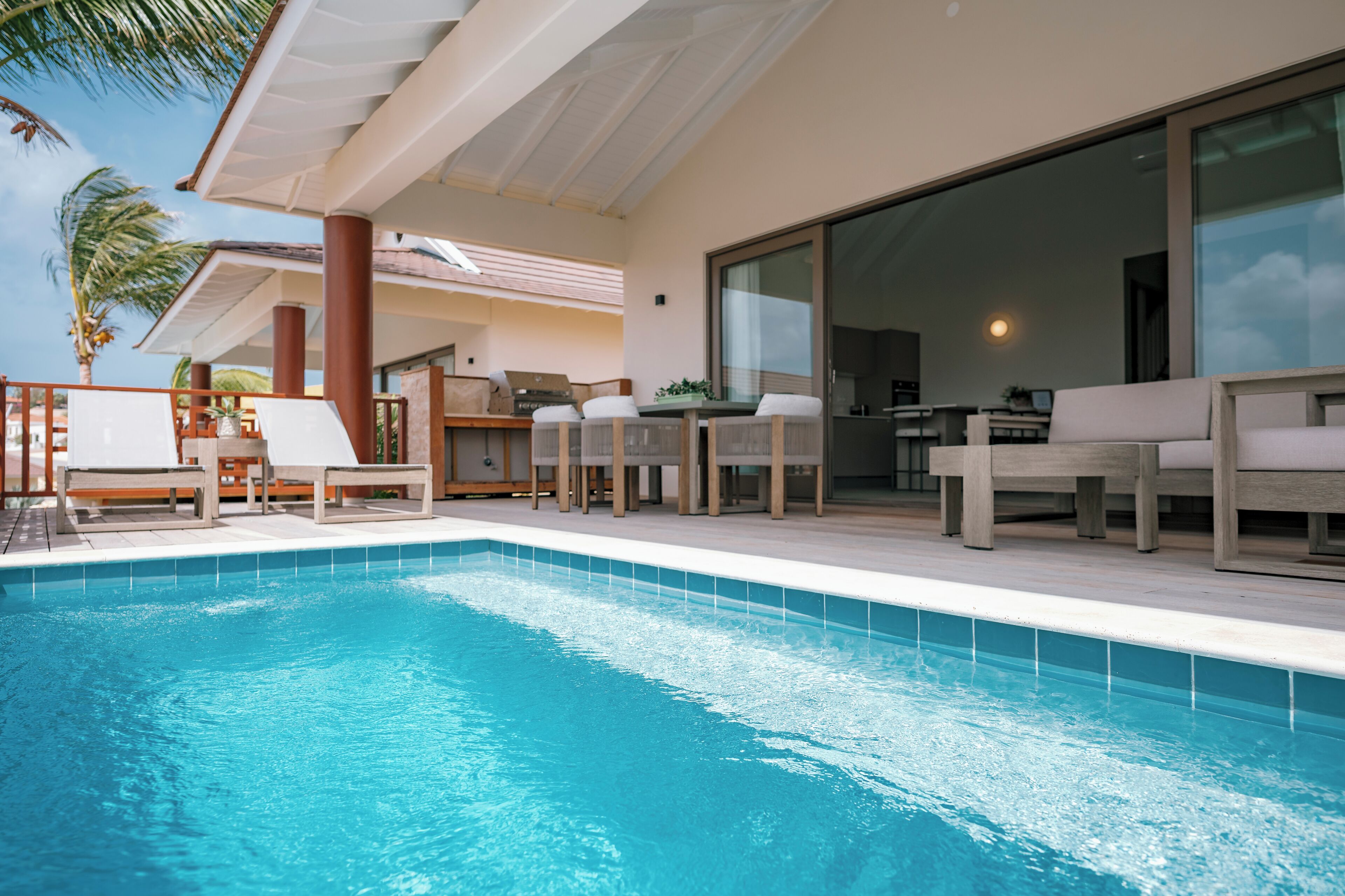 A swimming pool with lounge chairs, a dining area, and a large sliding glass door.