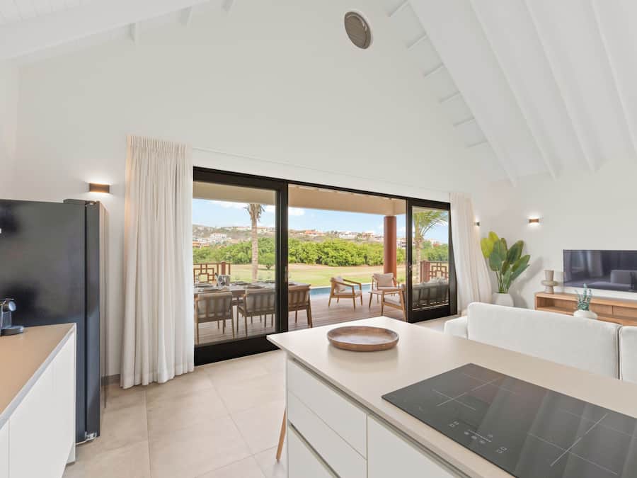 A modern kitchen with a large island, a dining area with outdoor seating, and a TV on the wall.