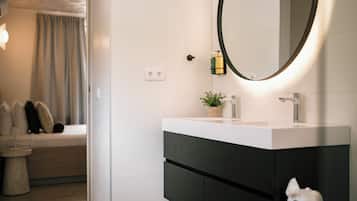 Un baño moderno con un lavamanos blanco, mueble oscuro y un espejo redondo con luz.