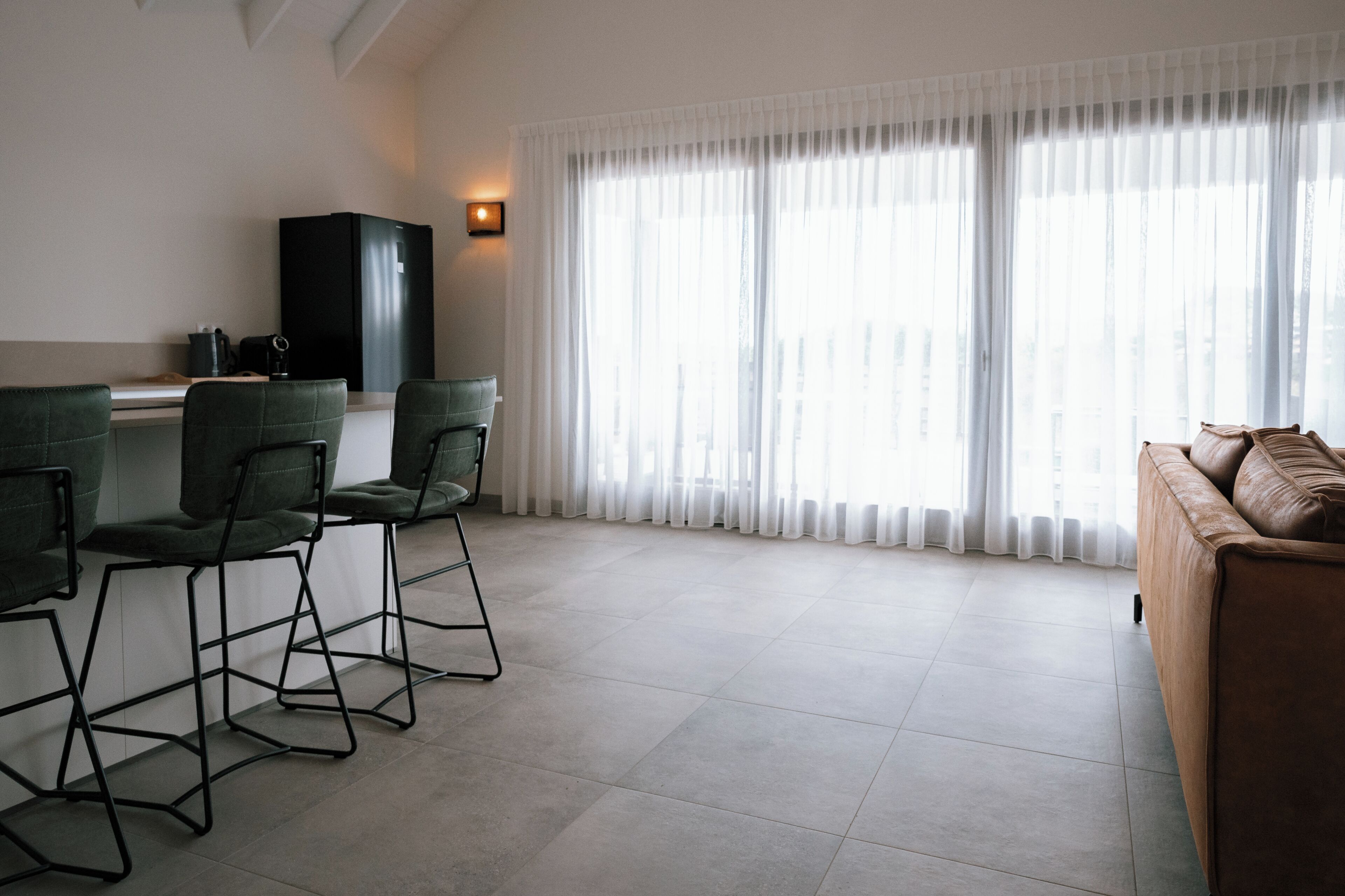 Una sala de estar moderna con un sofá, dos sillones, una mesa de centro, un armario negro y un ventanal con cortinas translúcidas.