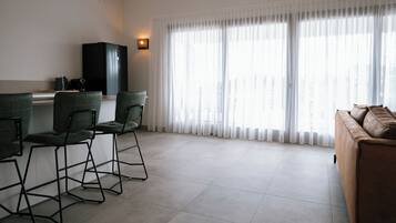 Una sala de estar moderna con un sofá, dos sillones, una mesa de centro, un armario negro y un ventanal con cortinas translúcidas.