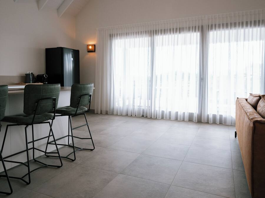 Una sala de estar moderna con un sofá, dos sillones, una mesa de centro, un armario negro y un ventanal con cortinas translúcidas.