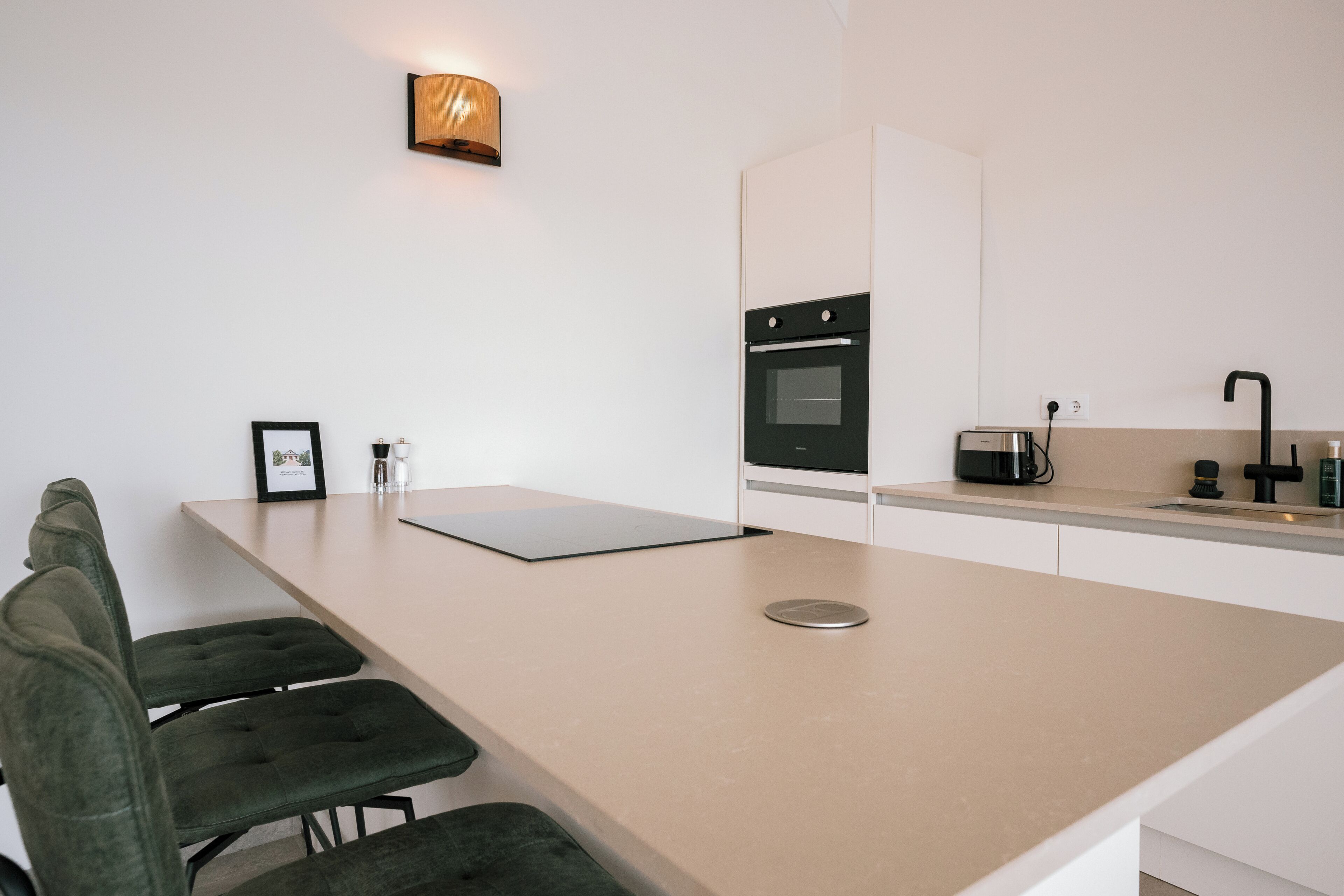 Una cocina moderna con una isla grande, armarios blancos, horno empotrado y cafetera.