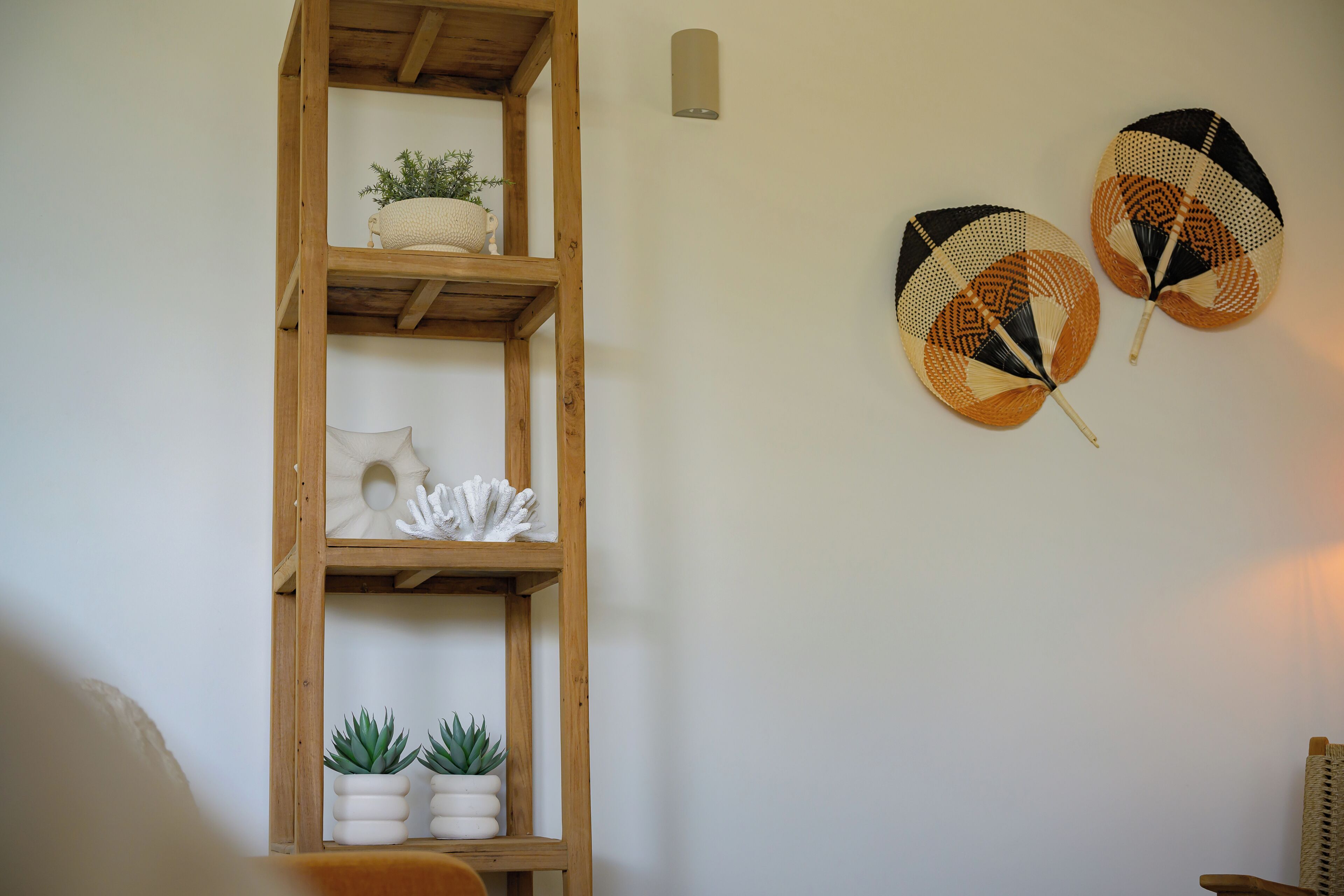A wooden shelf with decorative items and two woven fans on a plain wall.