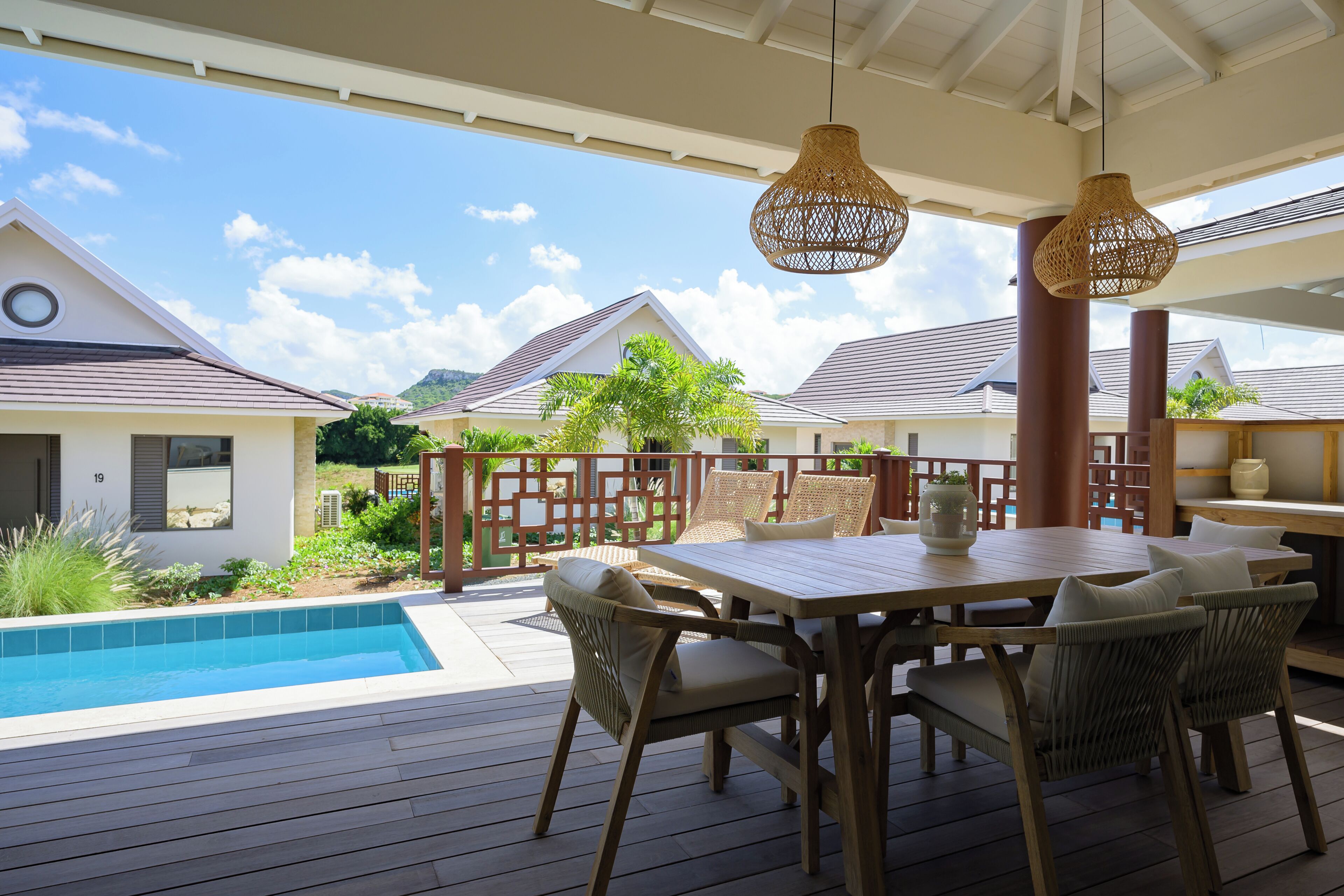 Una terraza de madera con piscina, muebles de exterior y vistas a casas al fondo.