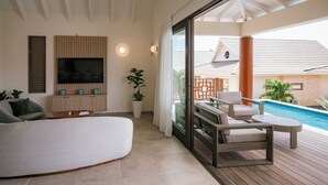 A modern living room with a flat-screen TV, a sofa, a coffee table, and a view of a swimming pool. - The Jazmyn - Blue Bay Golf & Beach Resort (Sint Michiel)