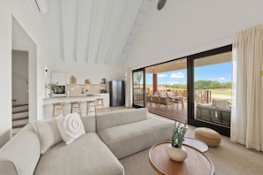 A modern living room with a sofa, a coffee table with a plant, and a view of an outdoor patio with a dining area. - The Jazmyn - Blue Bay Golf & Beach Resort (Sint Michiel)