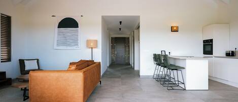 A modern interior with a sofa, a dining area with chairs, a kitchen, and a hallway.