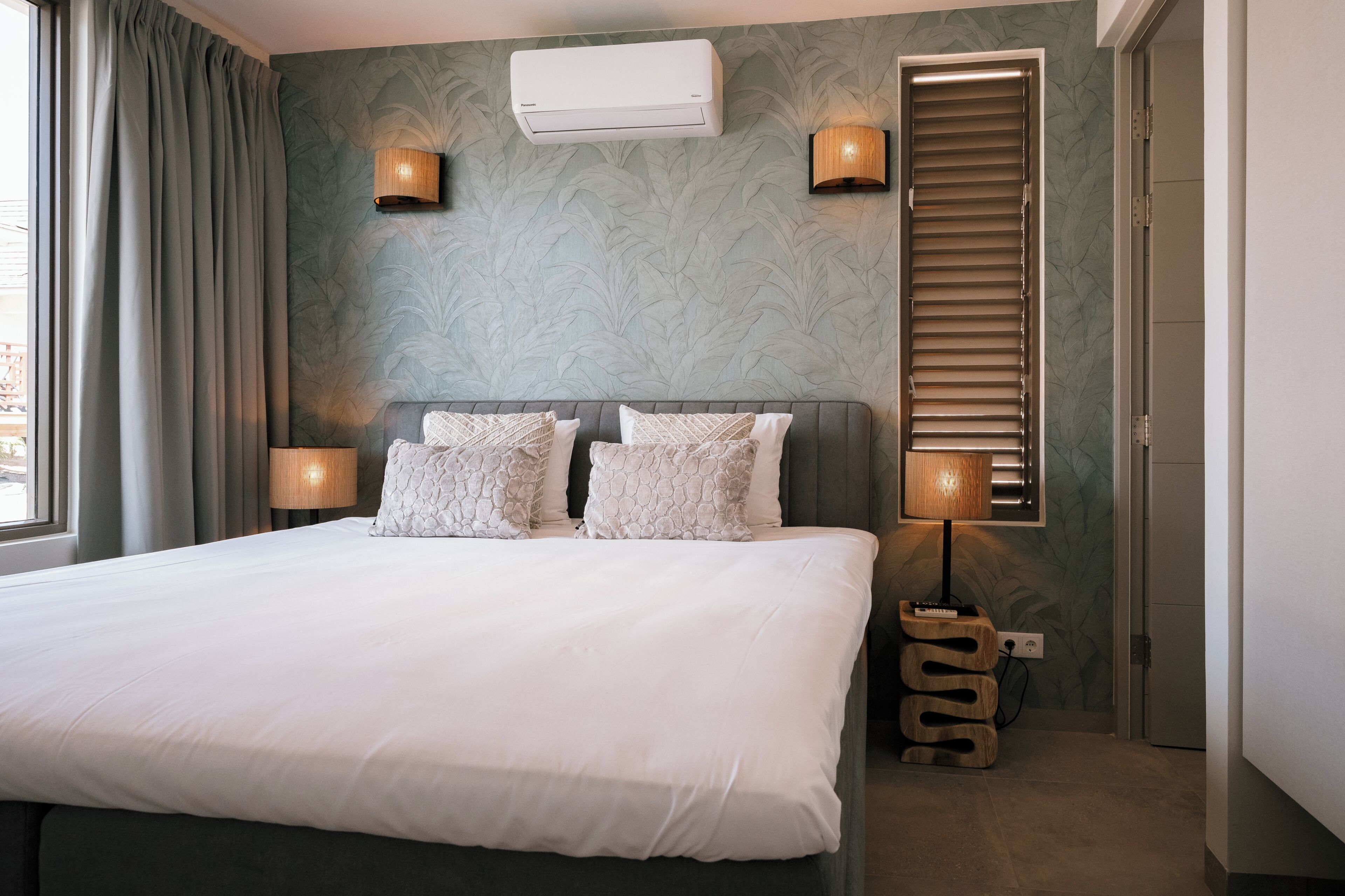 Quarto com cama, duas luminárias na parede, ar condicionado e mesa de cabeceira de madeira.