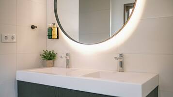 Un baño moderno con un lavamanos blanco, un espejo redondo y una planta en maceta.