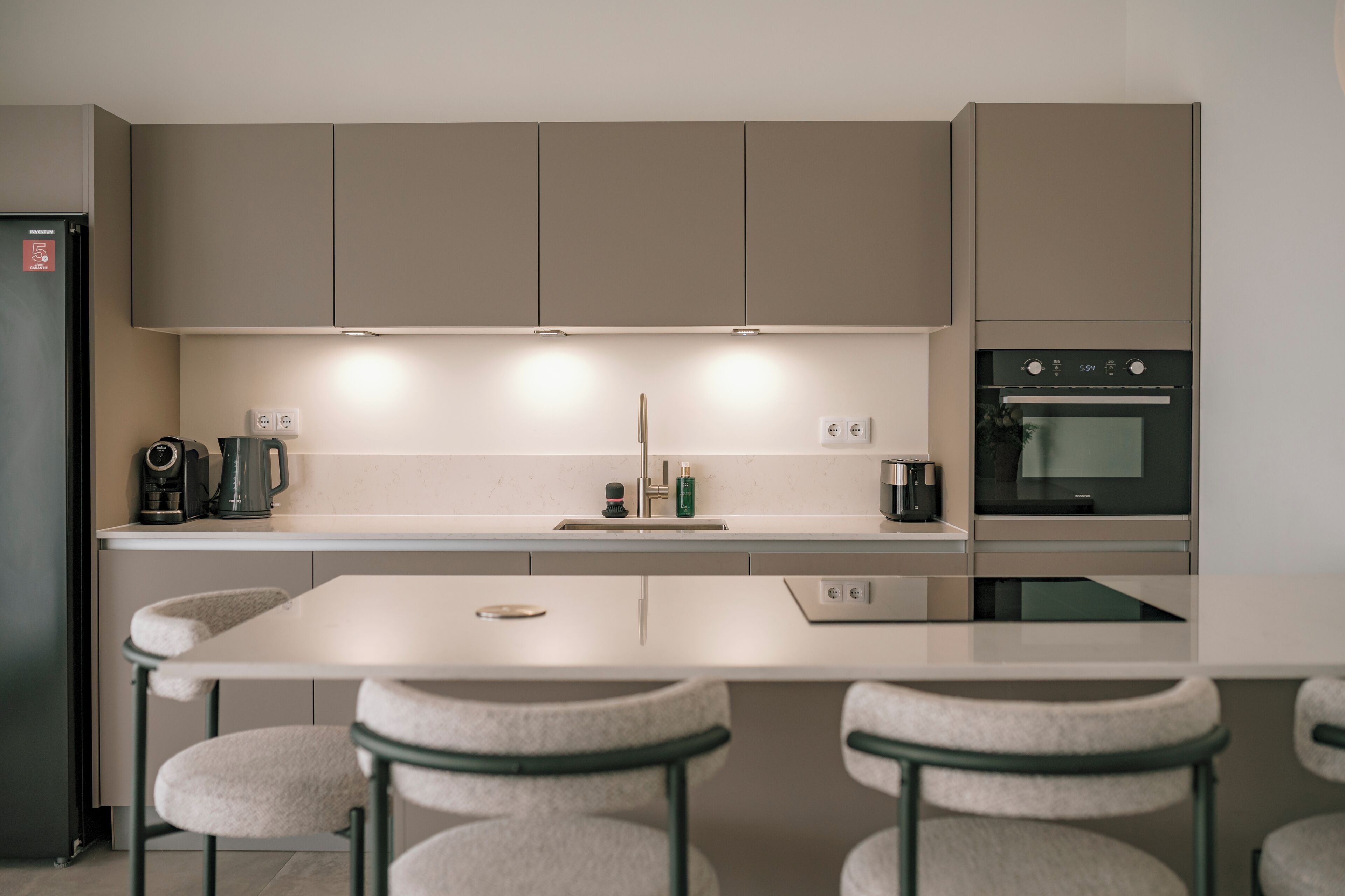 Una cocina moderna con una isla central, taburetes de bar, horno empotrado y cafetera.