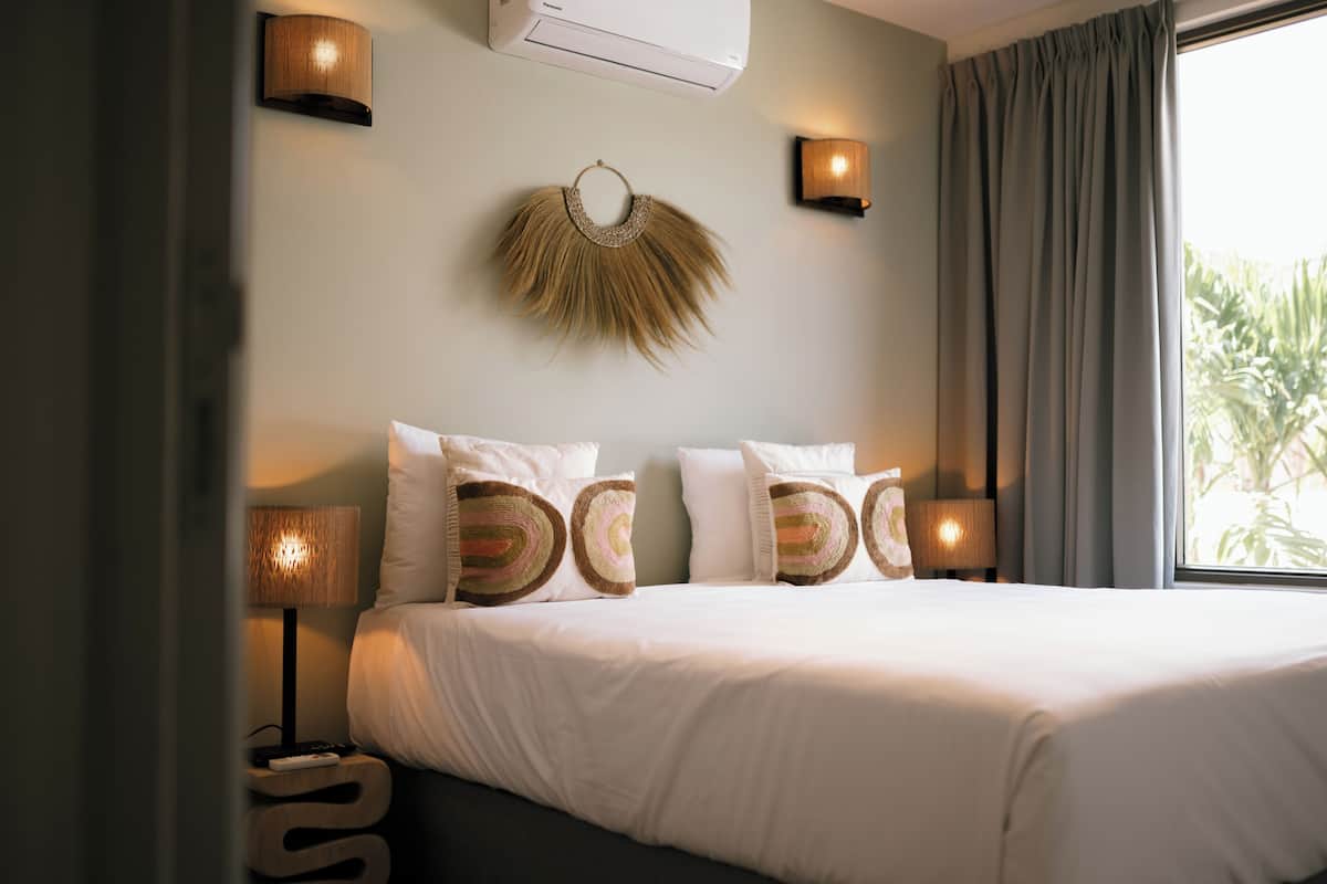 A bedroom with a bed, wall-mounted lamps, a wall decor, and a window with curtains.
