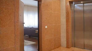 En moderne elevator, en gang med marmortæpper og et glimt af en stue med sofa og gardiner.
