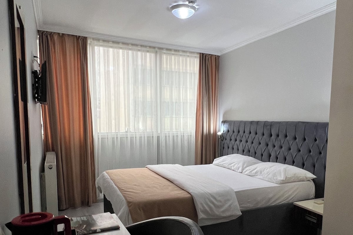 Habitación de hotel con cama, escritorio, silla, mesita de noche y ventana con cortinas.