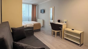 A modern hotel room with a sofa, a desk, a bed, a television, and a mirror. - BUYAR OTEL  (Samsun)