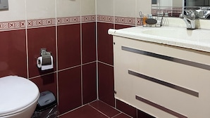 A bathroom with a toilet, a sink, a mirror, a towel rack with towels, and a trash bin. - BUYAR OTEL  (Samsun)
