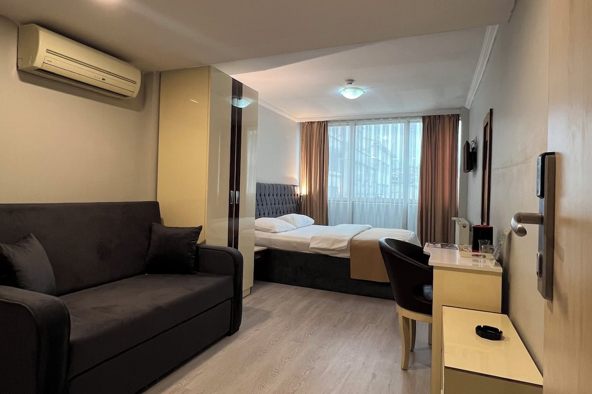 Una habitación de hotel con cama, sofá, escritorio y equipo de aire acondicionado.
