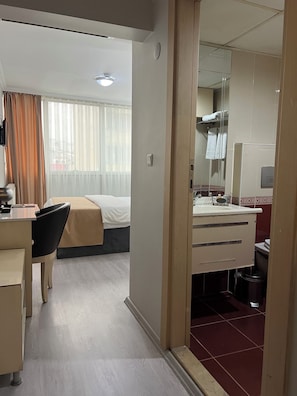 A hotel room with a bed, desk, chair, and a bathroom with a mirror and sink. - BUYAR OTEL  (Samsun)
