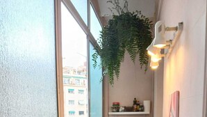 En smal balkon med et træbord, en hængende plante og udsigt til bygninger.