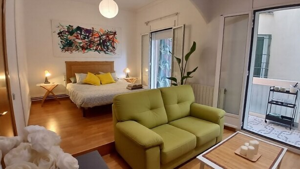 Et moderne værelse med en seng, en grøn sofa, et lille bord og et stort vindue.