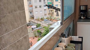 En balkon med udsigt over et boligområde, et lille udendørs siddeområde og et køkken med kaffemaskine.