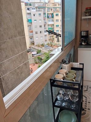 Un balcón con vistas a una zona residencial, un pequeño espacio de estar al aire libre y una cocina con cafetera.