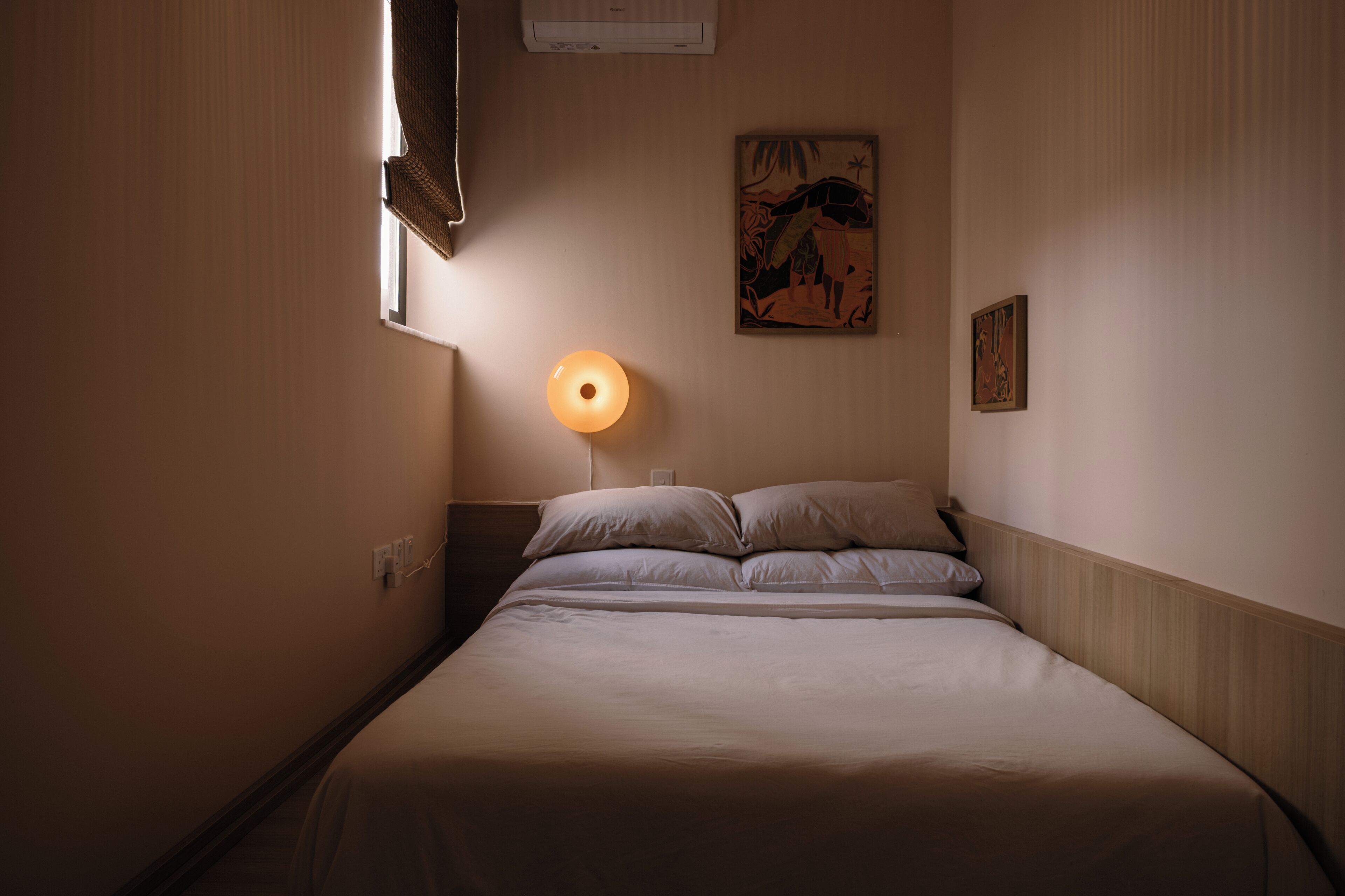Habitación de hotel con cama, aire acondicionado de pared, un cuadro y una lámpara.