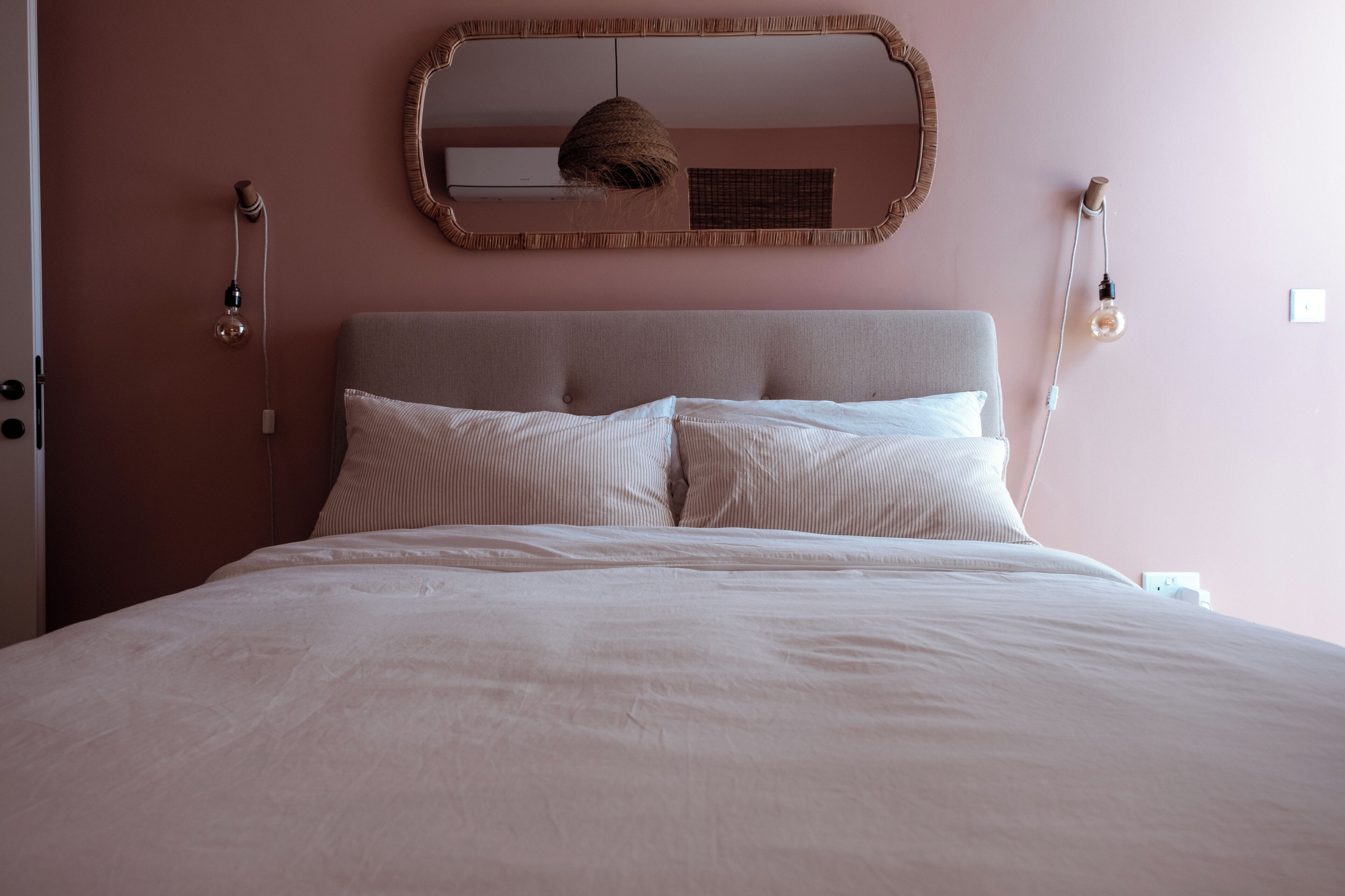 Un lit avec une tête de lit, deux appliques murales et un miroir au-dessus du lit.