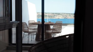 A balcony with wicker chairs and a table, overlooking a body of water and a hilly landscape. - Experience a brand-new seafront duplex penthouse in Ghadira Bay, featuring 2 bedrooms, 2 bathrooms, a fully equipped kitchen and two spacious terraces, both offering beautiful sea views just steps from the beach. (Il-Mellieħa)
