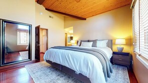 A bedroom with a bed, bedside tables, a nightstand, a mirror, a window with blinds, and a wooden ceiling. - Private Garage & Laundry, Views of Mammoth Rock, Welcomes Pets (Mammoth Lakes)